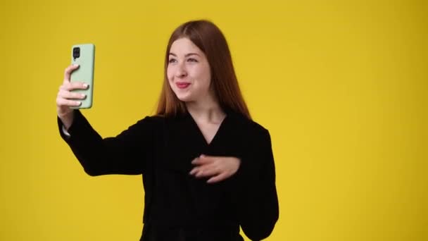 4K视频的可爱女孩使用手机和在黄色背景上挥手打招呼 情绪的概念 — 图库视频影像