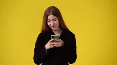 Sarı arka planda telefonunu kullanan bir kadının 4K videosu. Duygu kavramı.