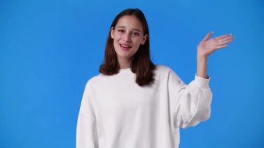 Mavi arka planda hoş bir kızın el salladığı 4K yavaş çekim videosu. Duyguların kavramı.