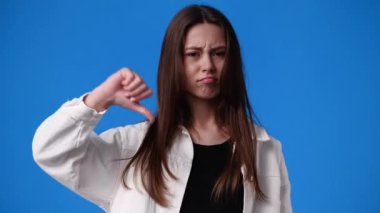 Mavi arka planda küçük bir kızın baş parmağını gösteren 4K yavaş çekim videosu. Olumsuz duygu kavramı.