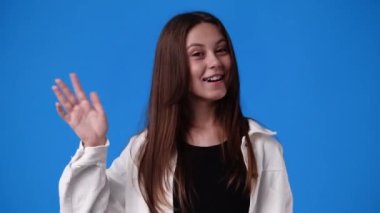 Mavi arka planda hoş bir kızın el salladığı 4K yavaş çekim videosu. Duyguların kavramı.