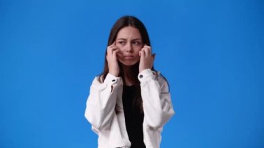 Mavi arka planda baş ağrısı çeken bir kızın 4K yavaş çekim videosu. Duyguların kavramı.