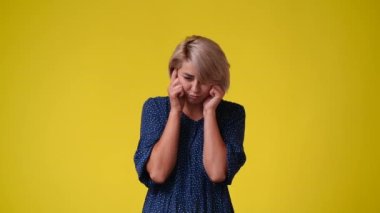 Sarı arka planda baş ağrısı çeken bir kızın 4K yavaş çekim videosu. Duyguların kavramı.