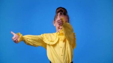 Mavi arka planda baş parmağını gösteren bir kızın 4K yavaş çekim videosu. Duyguların kavramı.