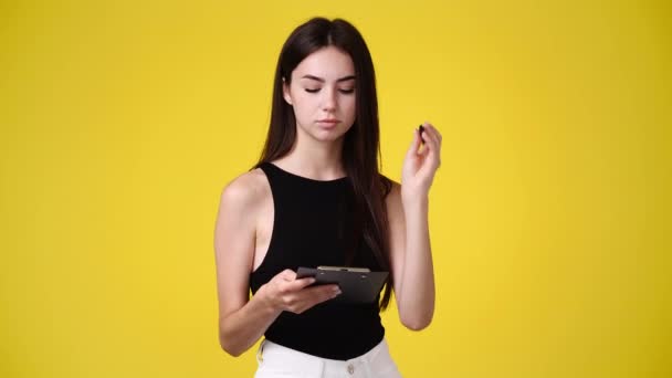 黄色の背景にノートパッドを持つ1人の女の子の4Kスローモーションビデオ 感情の概念 — ストック動画