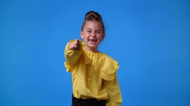 Bir kızın kamerayı işaret edip mavi arka planda dilini gösterdiği 4k yavaş çekim videosu. Duyguların kavramı.