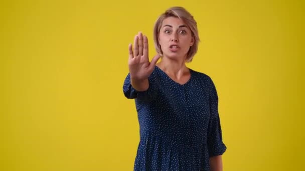 黄色の背景の上に停止標識を示す1人の少女の4Kスローモーションビデオ 感情の概念 — ストック動画