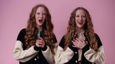 İki ikiz kızın 4K videosu pembe arka planda bir şey için heyecanlı. Duyguların kavramı.