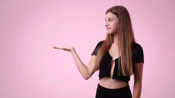 4Kスローモーションビデオの可愛い女の子が左を向いてピンクの背景に親指を立てています 感情の概念 — ストック動画