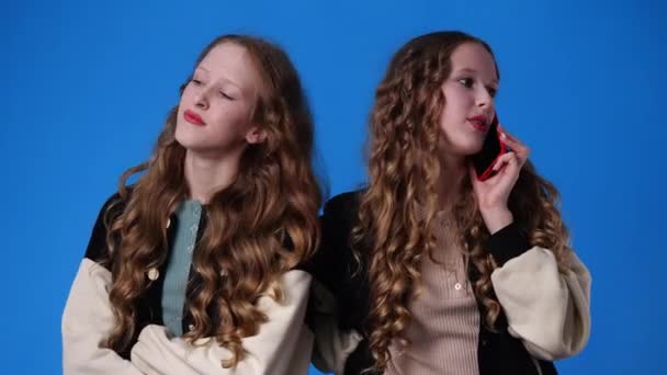 青い背景の上で電話で話している双子の女の子の4Kビデオ 感情の概念 — ストック動画