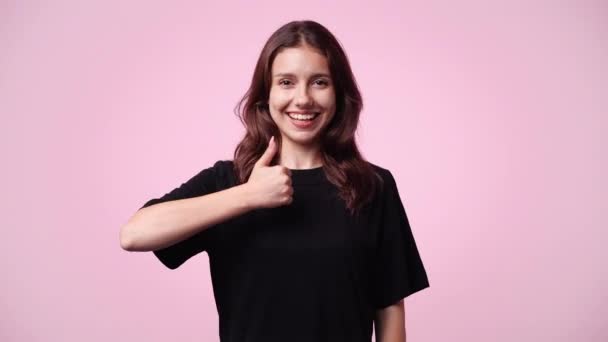 ピンクの背景に親指を出す1人の少女の4Kスローモーションビデオ 感情の概念 — ストック動画