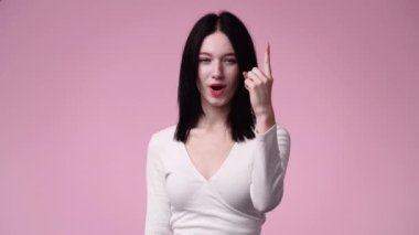 4K yavaş çekim videosu. Pembe arka planda büyük gözleri olan bir kız el kaldırıyor. Duyguların kavramı.