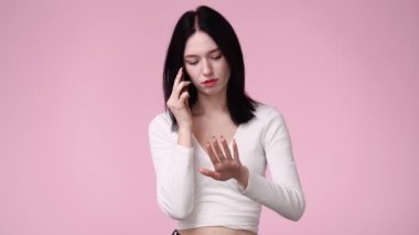Pembe arka planda telefonla konuşan bir kızın 4K yavaş çekim videosu. Duyguların kavramı.