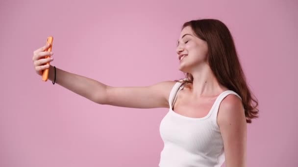 ピンクの背景でビデオコールを持っている1人の女の子の4Kスローモーションビデオ 感情の概念 — ストック動画