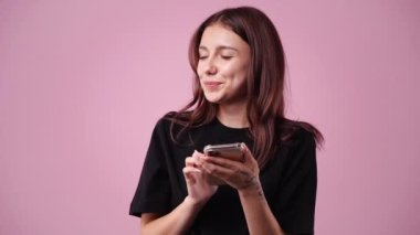 Pembe arka planda telefonunu kullanan bir kızın 4K yavaş çekim videosu. Duyguların kavramı.
