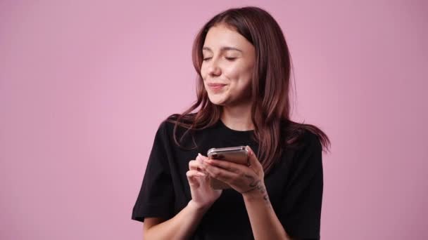 ピンクの背景の上に彼女の携帯電話を使用して1人の女の子の4Kスローモーションビデオ 感情の概念 — ストック動画