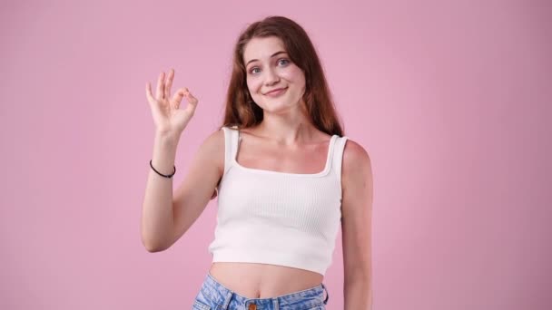 ピンクの背景にOkの看板を見せる可愛い女の子の4Kスローモーション動画 感情の概念 — ストック動画