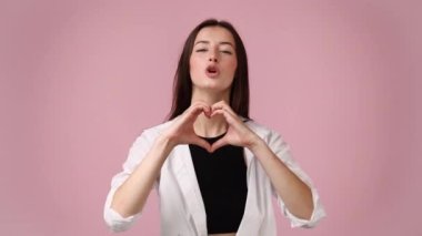Kızın ellerini pembe arka planda gezdirip kalp şeklini değiştirdiği 4K yavaş çekim videosu. Aşk duyguları kavramı.