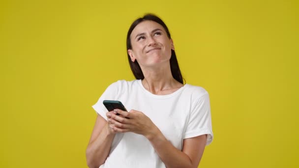 4K慢动作视频一个女孩在黄色背景下使用她的手机 情绪的概念 — 图库视频影像