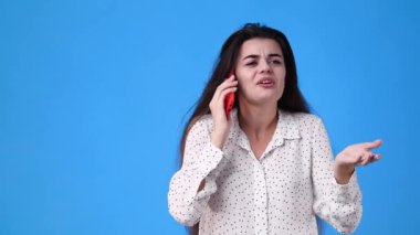 Mavi arka planda telefonla konuşan bir kızın 4K videosu. Duyguların kavramı.