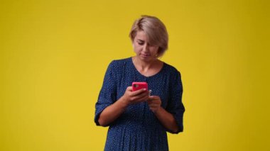 Sarı arka planda telefonunu kullanan bir kadının 4K yavaş çekim videosu. Duyguların kavramı.