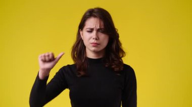 Sarı arka planda baş parmağını gösteren 4K yavaş çekim videosu. Olumsuz duygu kavramı.