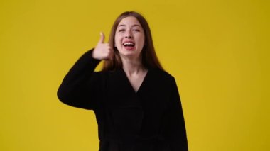 4k slow motion video of one girl showing thumb up over yellow background. Concept of emotions.
