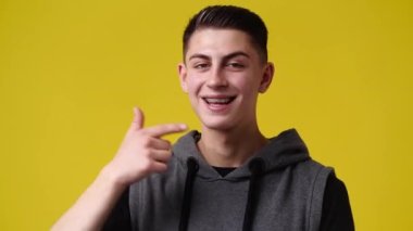 4k slow motion video of smiling man pointing at right and showing thumb up on yellow background. Concept of emotions.