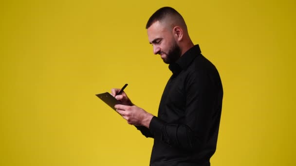 黄色の背景の上にノートを取る1人の男の4Kスローモーションビデオ 感情の概念 — ストック動画