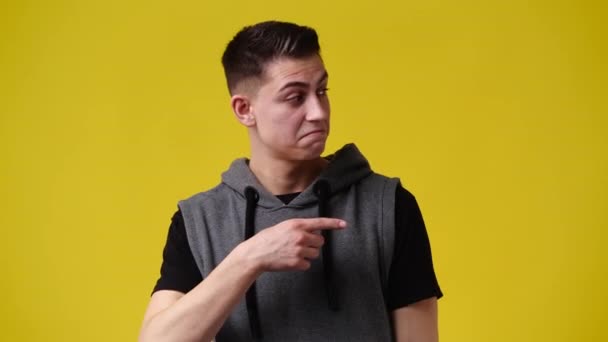 1人の男が右を指して親指を黄色の背景に表示する4Kのスローモーションビデオ 感情の概念 — ストック動画