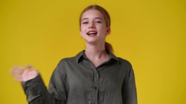 4k slow motion video of one girl waving hello on yellow background. Concept of emotions.