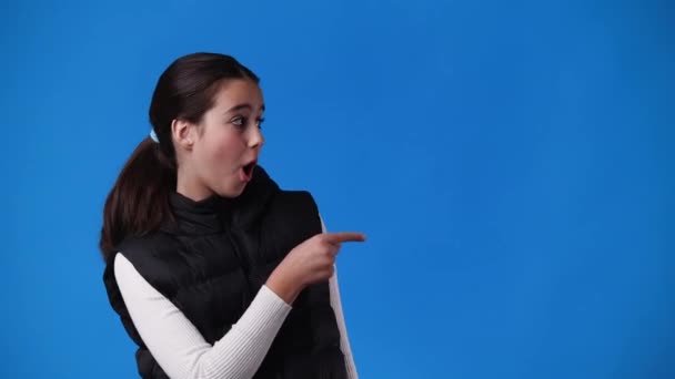 1人の女の子が右を向いて親指を青の背景の上に見せる4Kビデオ 感情の概念 — ストック動画