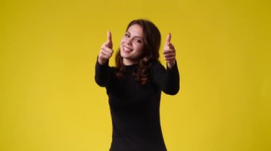 4k video of one girl showing thumbs up over yellow background. Concept of emotions.