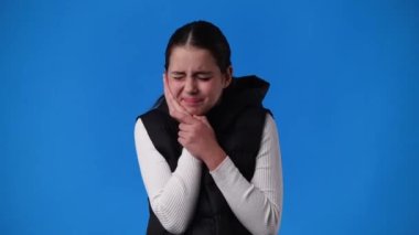 4k video of one girl having toothache on blue background. Concept of ill girl.