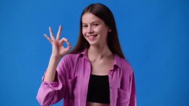 4k video of cute girl showing OK sign on blue background. Concept of emotions.