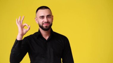 Sarı arka planda OK işareti gösteren bir adamın 4k yavaş çekim videosu. Duyguların kavramı.