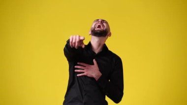 4k video of one man pointing at the camera and laughing over yellow background. Concept of emotions.