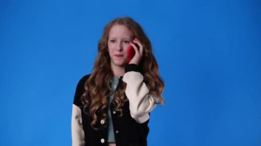 4k slow motion video of one girl talking over the phone on blue background. Concept of emotions.