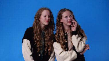 4k slow motion video of twin girls talking over the phone on blue background. Concept of emotions.