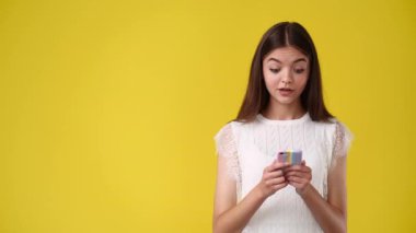 4k slow motion video of one girl with phone in hand pointing at left side over yellow background. Concept of emotions.