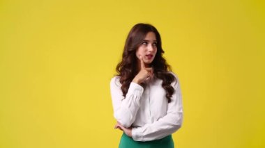 Sarı arka planda kurnaz yüz ifadesi olan bir kızın 4k yavaş çekim videosu. Fikirleri olan kız kavramı.