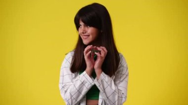 Sarı arka planda kurnaz yüz ifadesi olan bir kızın 4K videosu. Fikirleri olan kız kavramı.