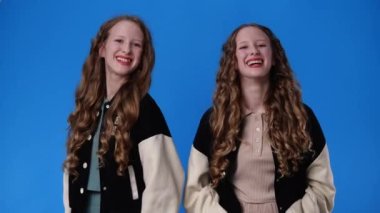 4k slow motion video of two twin girls making hearts with their fingers over blue background. Concept of emotions.