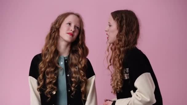 ピンクの背景についていくつかの議論を持っている双子の女の子の4Kスローモーションビデオ 感情の概念 — ストック動画