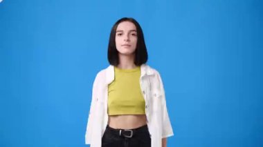 4k video of one girl pointing at the camera and showing thumbs up over blue background. Concept of emotions.