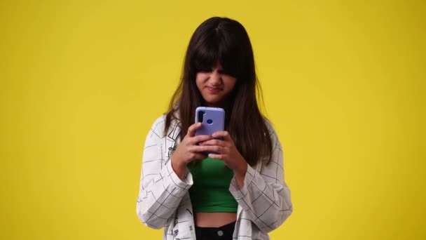 黄色の背景色の上に携帯電話を使って1人の女の子の4Kスローモーションビデオ 感情の概念 — ストック動画