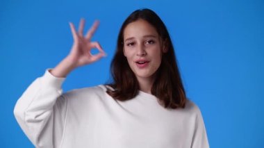 4k slow motion video of cute girl showing OK sign on blue background. Concept of emotions.