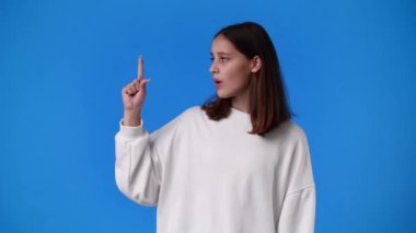 4k slow motion video of girl raising hands in surprise looking at camera with big eyes on blue background. Concept of countdown.