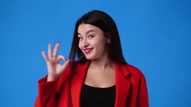 4k slow motion video of cute girl showing OK sign on blue background. Concept of emotions.