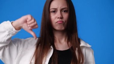 4k slow motion video of one girl with negative facial expression showing thumb down over blue background. Concept of emotions.